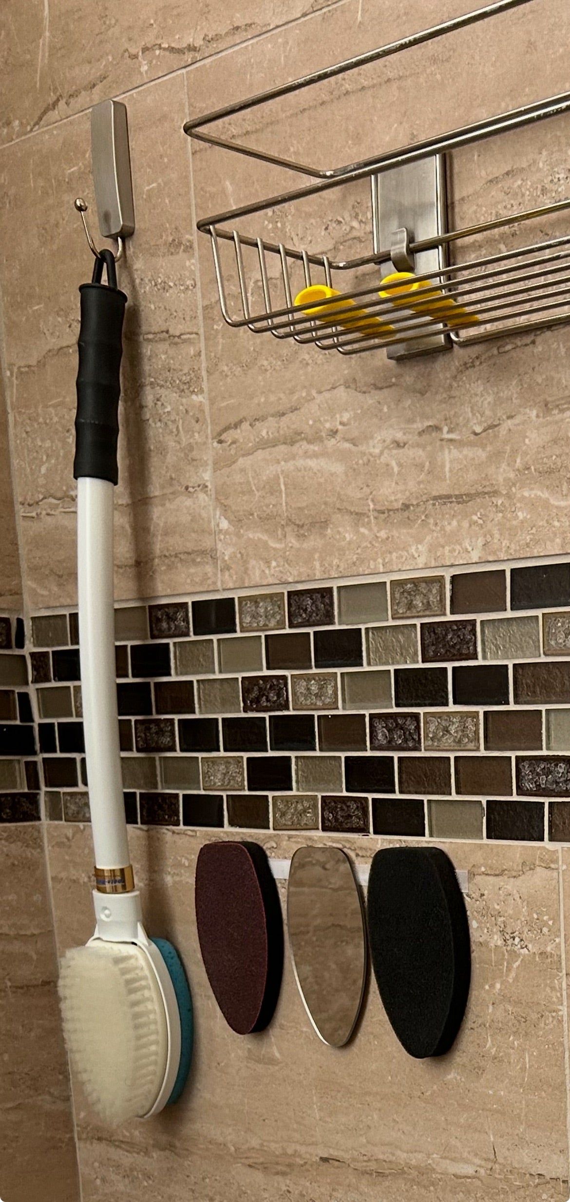 Cleaning brush with black handle and white bristles on a tiled wall with a metal rack above.